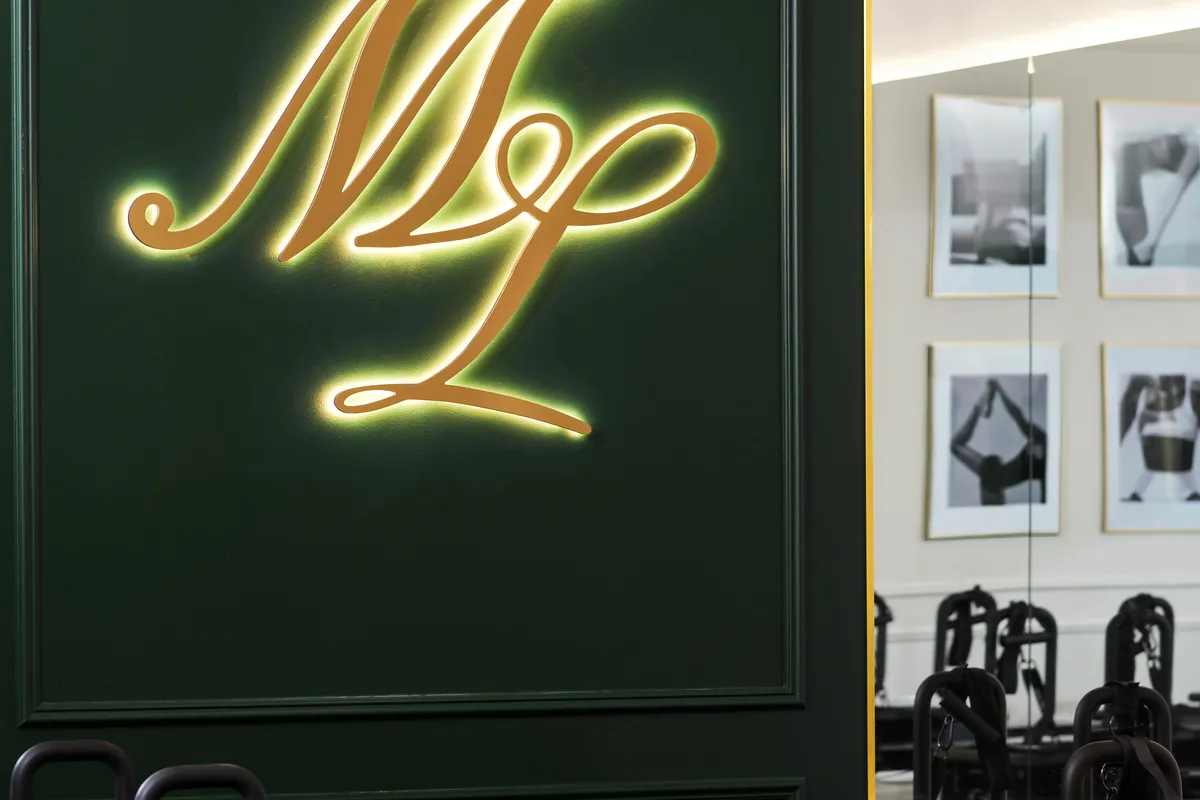 The backlit gold ML monogram glowing on the studio's green wall beside a gold-framed mirror